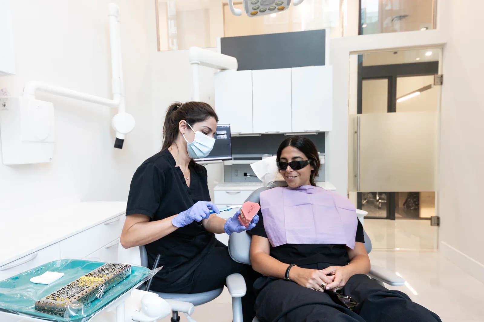 A dental hygienist showing a smiling patient how to brush during a cleaning at Dentistry on Gloucester in downtown Toronto